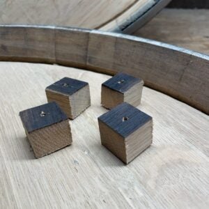 Four small wooden cubes with one blackened face and holes in the center, placed inside a wooden barrel top.