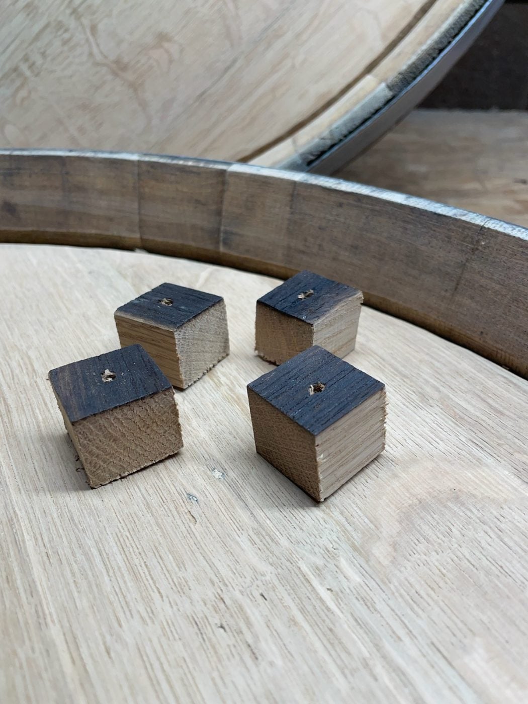 Four small wooden cubes with one blackened face and holes in the center, placed inside a wooden barrel top.