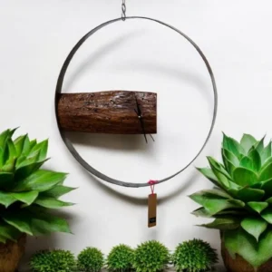 Hanging wall clock made from a log and metal ring, surrounded by green potted plants and small shrubs against a white background.