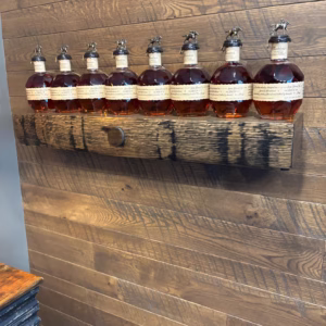 A row of Blanton's bourbon bottles displayed on a rustic wooden shelf mounted on a wood-paneled wall with warm brown tones.